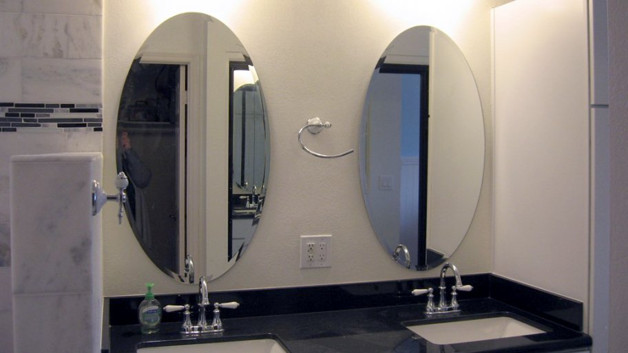 double mirror vanity with dark countertop and light cabinets